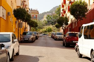 Sunny urban street with colorful buildings and parked cars, offering a Mediterranean vibe.