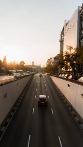 A solitary car drives on an urban road at sunrise, capturing a serene cityscape moment.